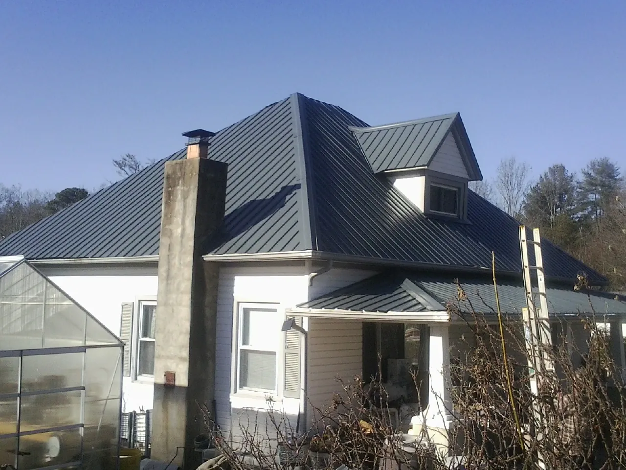 Dark blue standing seam metal roof on a white farmhouse with dormer — Slate & Tile Roof Repair by Roofing Brothers in Rachel