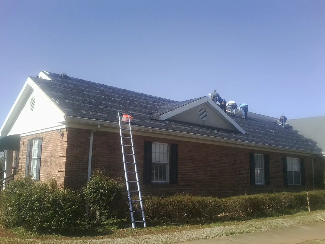 Crew tearing shingles off a brick ranch roof with a ladder set — Emergency Roof Repair work by our crew in Rachel