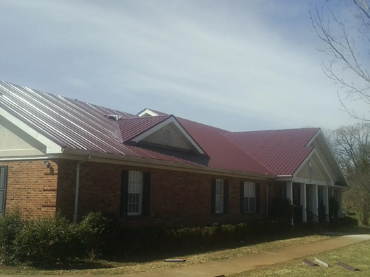 Red metal roof with gabled entries on a long brick building, from a Hail Damage Roof Repair job in Rachel