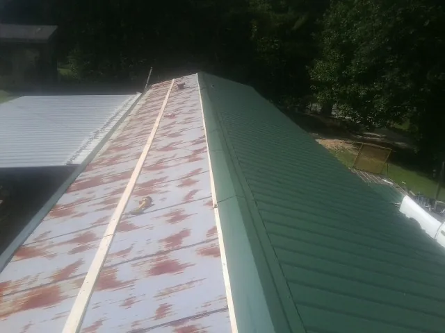 Old rusted panels beside newly installed green metal roofing — Wind Damage Roof Repair by Roofing Brothers in Rachel