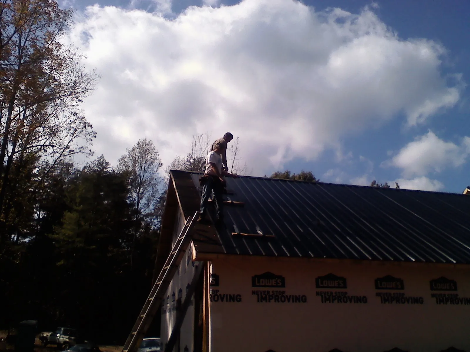 Roofer fastening dark metal panels high against a cloudy sky, from a Roof Inspection job in Rachel
