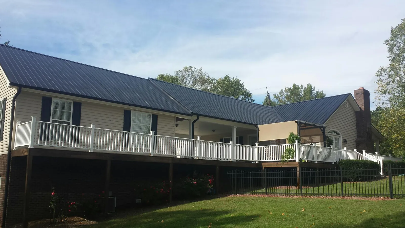 Black metal roof above a long white railed deck on a hillside home in Rachel