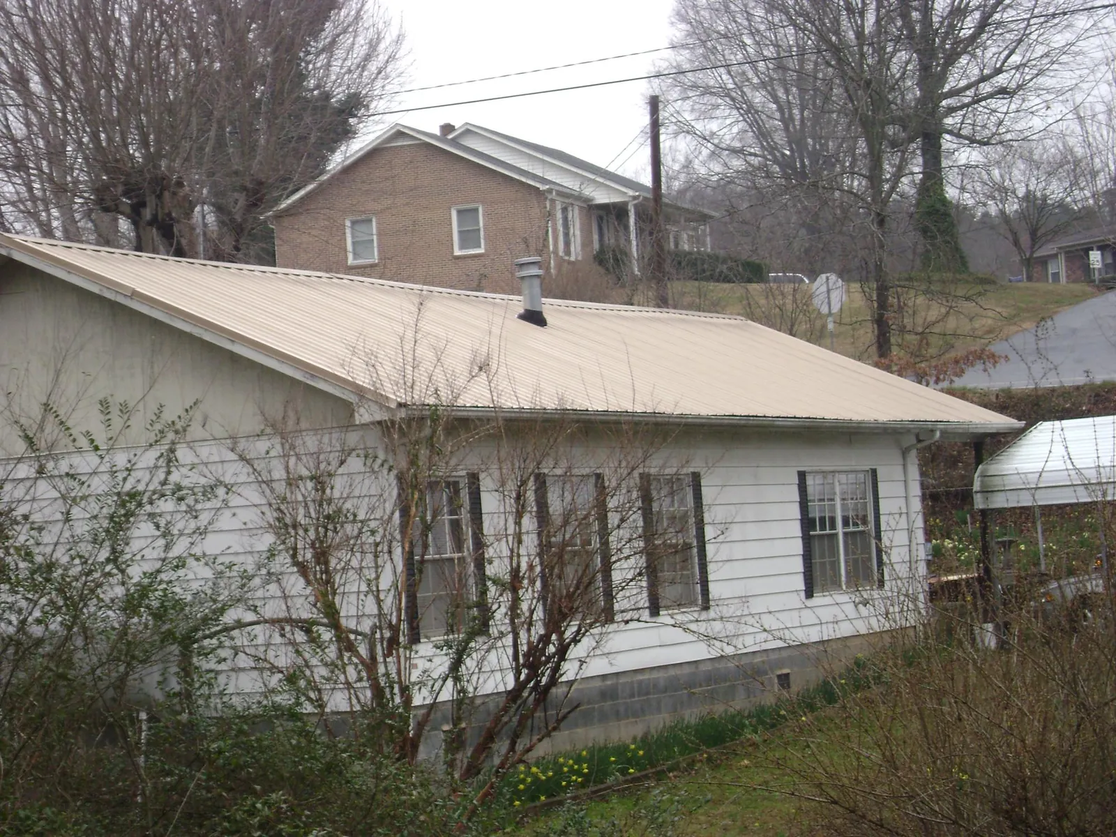 Tan metal roof on a white sided house set into a hillside — Commercial Roofing by Roofing Brothers in Rachel