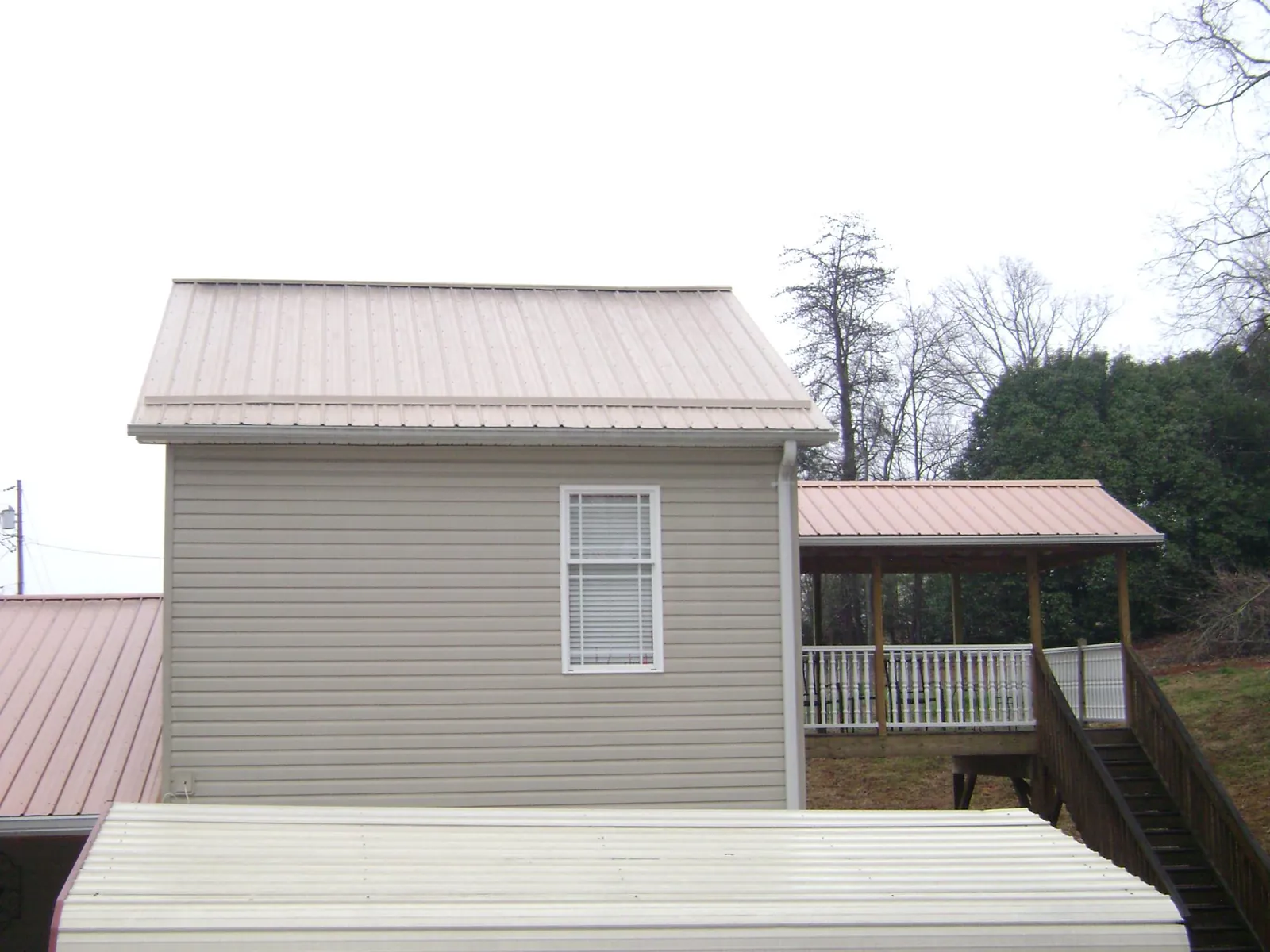 Tan metal roofs on a two story addition and attached porch, from a Roof Replacement job in Rachel